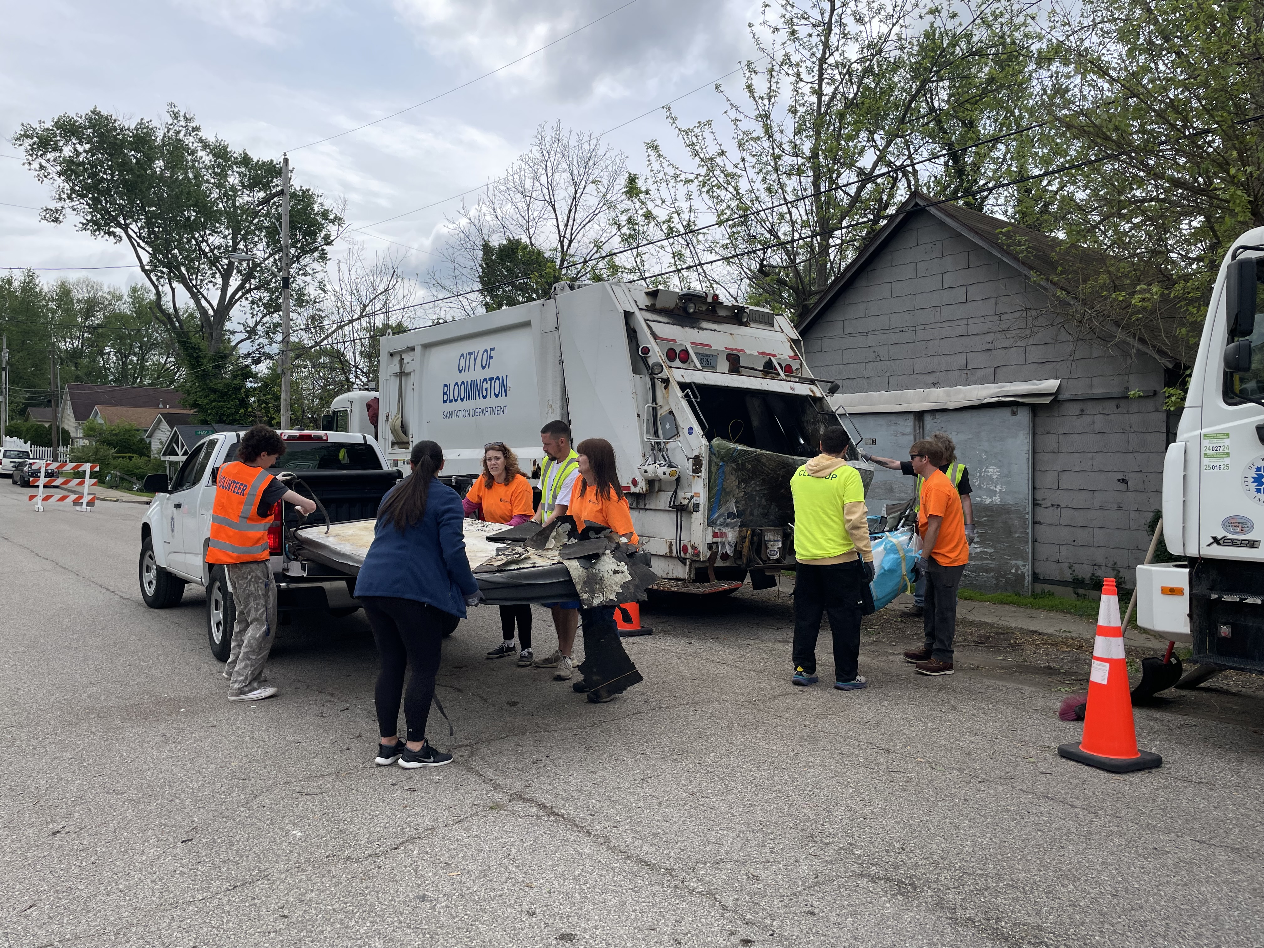 a group of people unloading trash from a pickup truck into a trash truck